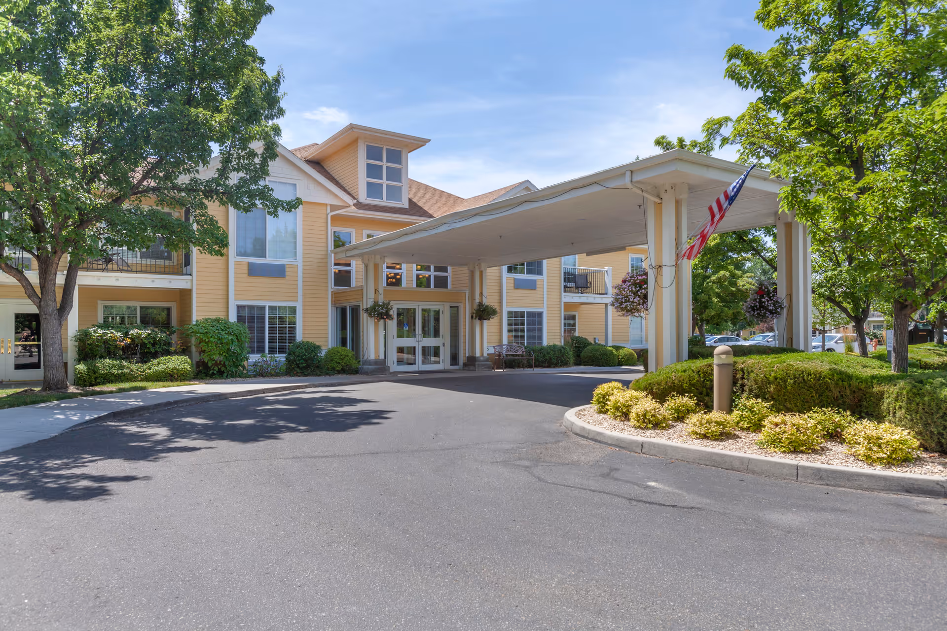 Yellow senior living facility entrance with a covered porte-cochere and landscaping.