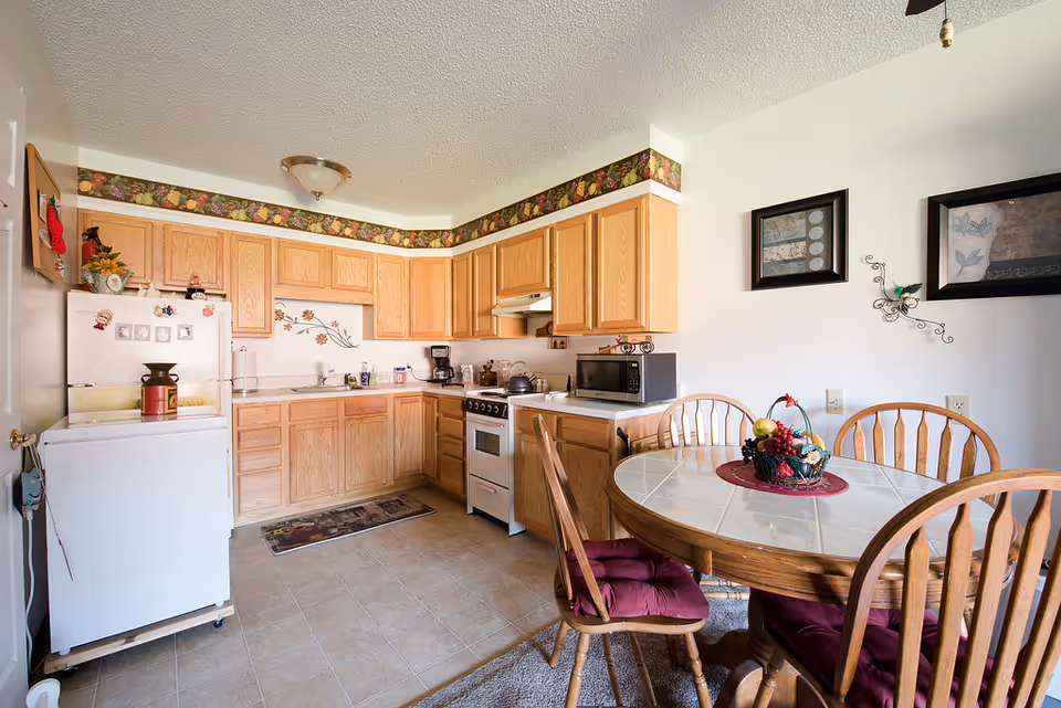 Bright kitchen and dining nook with oak cabinets, a round glass-top dining table with four chairs, refrigerator, stove, and microwave.