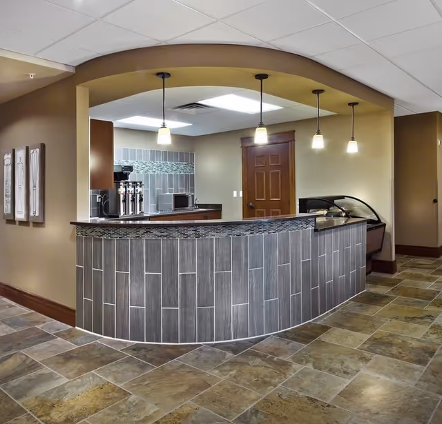 Curved tiled service counter with pendant lights, a coffee station and display case in a common area.