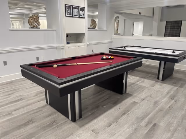 A bright indoor game room featuring a burgundy-felt pool table and an air hockey table on gray wood flooring.