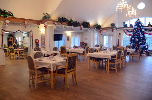 Spacious dining room with tables and chairs, set for a meal and decorated for Christmas including a large tree.