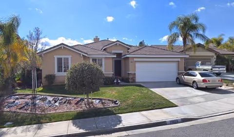 Front exterior of a single-story beige house with a two-car garage and palm trees.