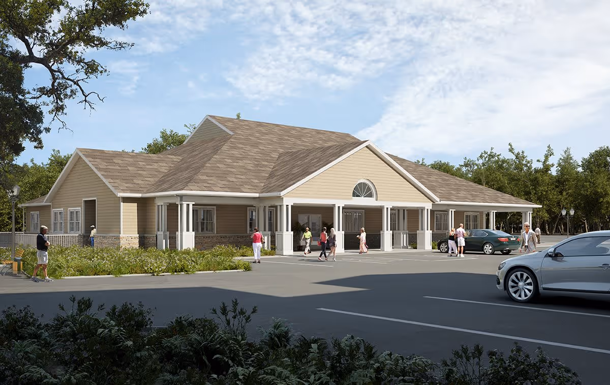Exterior view of a single-story senior living facility building with beige siding and a brown shingled roof. Several people are walking and standing near the entrance and parking lot, with cars parked nearby. Trees and greenery surround the area under a partly cloudy sky.