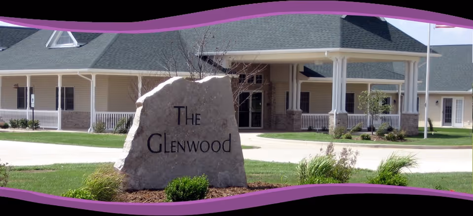 A large stone sign reading "The Glenwood" sits on landscaped grass in front of the entrance to a single-story assisted living building.
