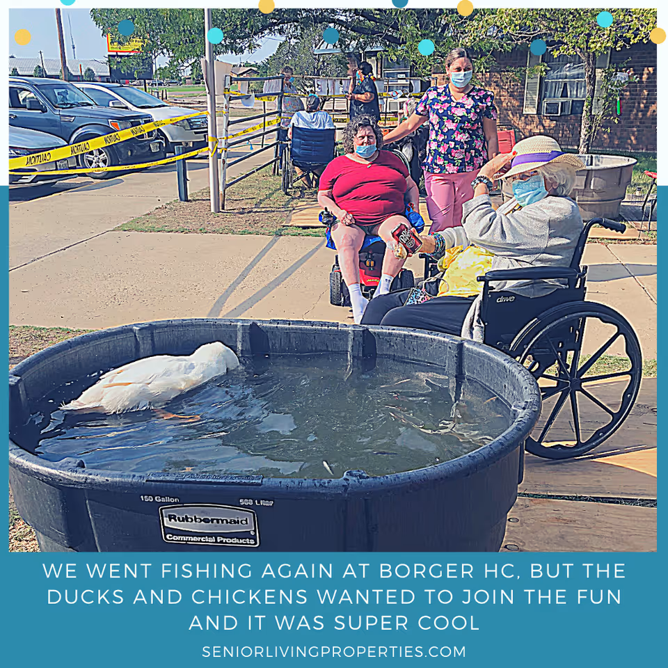 Several people, including elderly individuals in wheelchairs and a caregiver wearing a mask, are outdoors near a large black Rubbermaid tub filled with water where a white duck is swimming. Yellow caution tape is visible in the background along with parked cars and a brick building.
