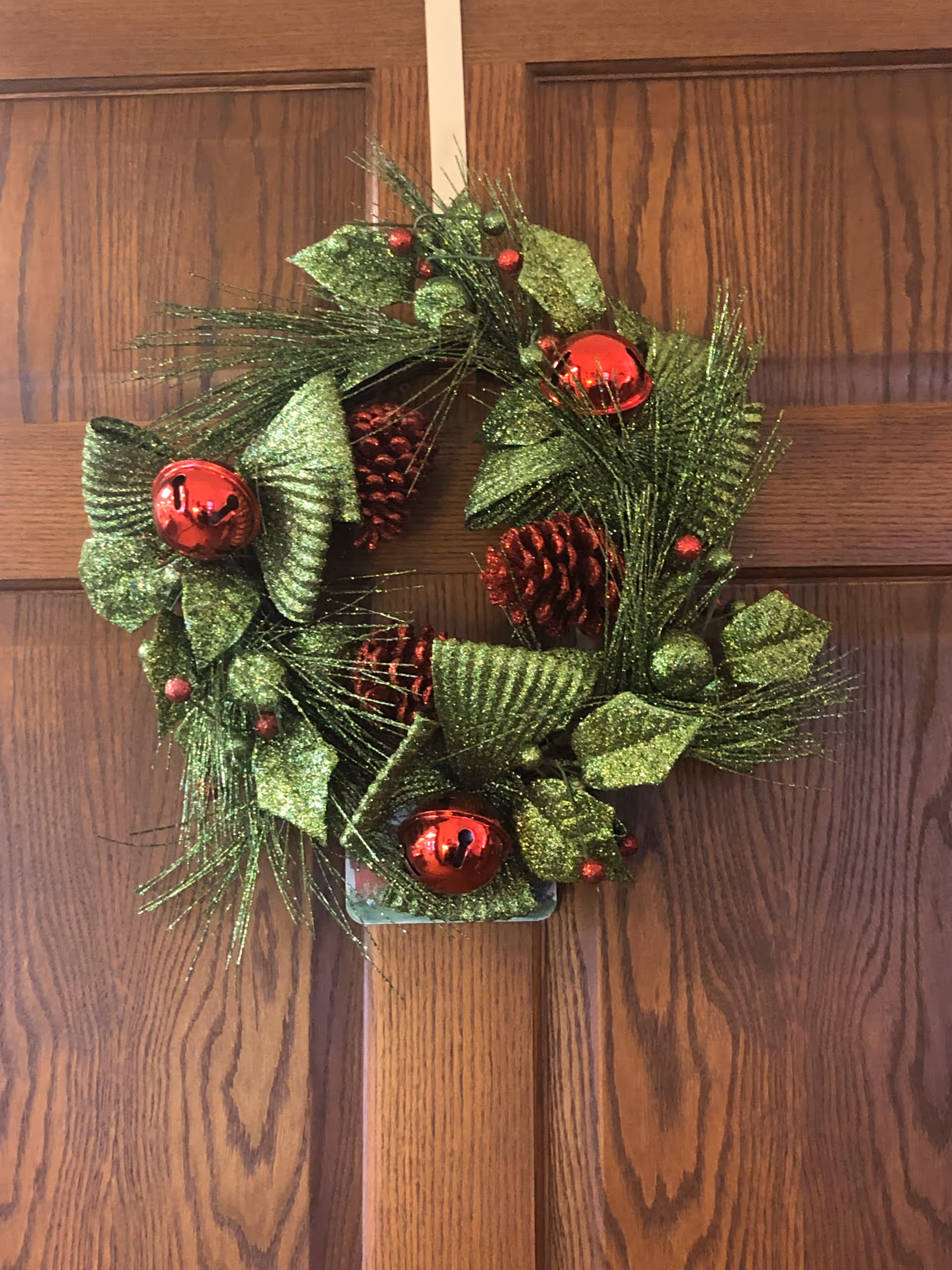 Green glittery Christmas wreath with red ornaments hanging on a wooden paneled door.