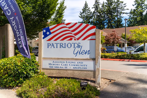 Entrance sign for Patriots Glen assisted living and memory care community with an American flag design, landscaping, and the facility building in the background.