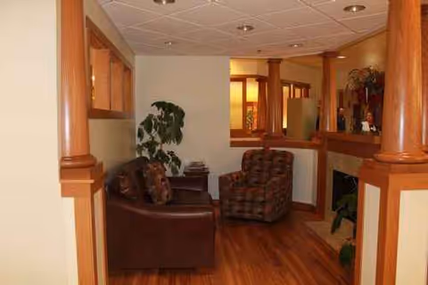 Cozy senior living lounge with brown seating, wooden columns, and a fireplace.