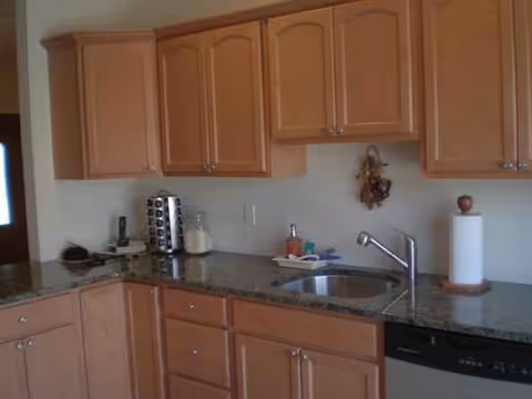 Wooden kitchen cabinets line a granite countertop with sink and small appliances.