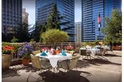 Rooftop terrace with round dining tables set with napkins, potted flowers, and city skyscrapers in the background.