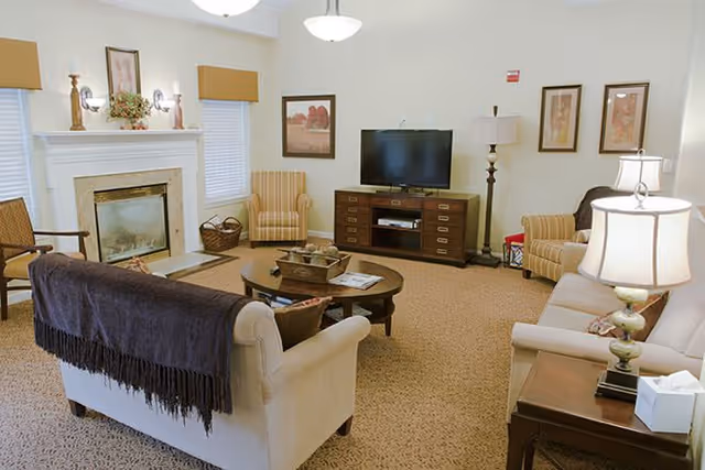Comfortable communal living room with sofas and armchairs arranged around a coffee table, a fireplace, and a TV on a media cabinet.
