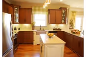 Bright kitchen with wooden cabinets, a white island in the center topped with a bowl of lemons, stainless steel refrigerator, dishwasher, and a window above the sink letting in natural light.