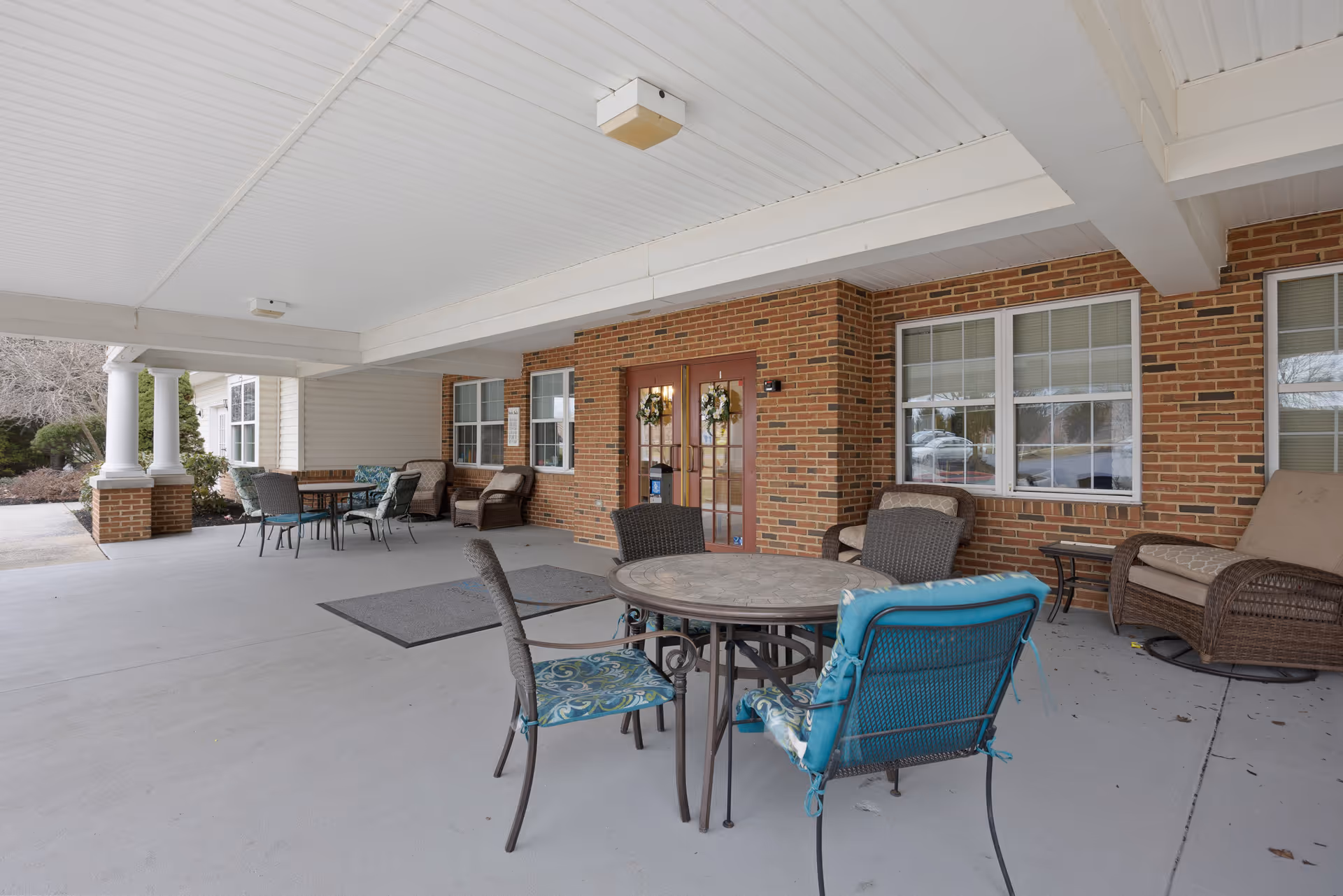Covered entry patio with round table and chairs, wicker seating, and double doors set in a brick exterior.