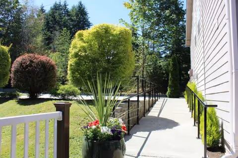Sunny outdoor walkway along the building with a ramp, planters, and greenery.