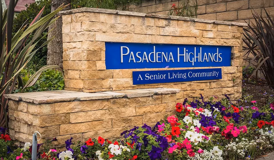 Stone sign for Pasadena Highlands, a senior living community, surrounded by colorful flowers and greenery.