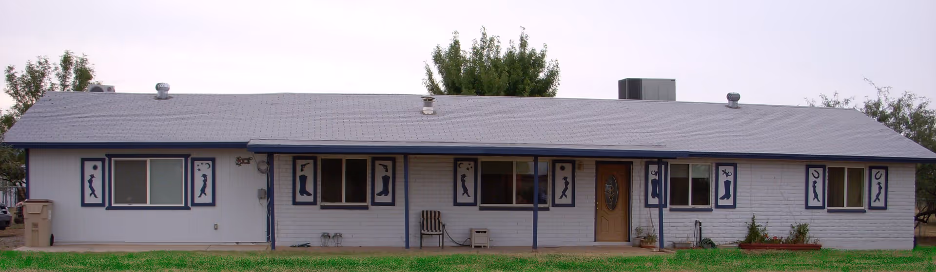 Long single-story ranch-style building front with blue trim, multiple windows, a central entry door and a grassy lawn.