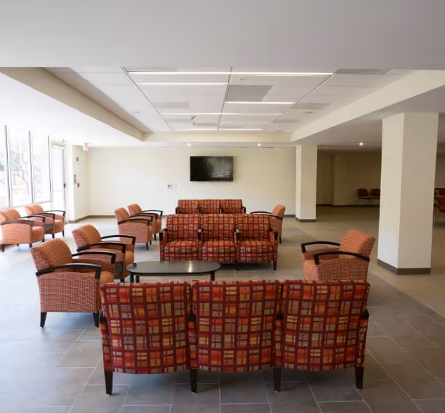 A spacious senior living lounge with red plaid chairs arranged around coffee tables.
