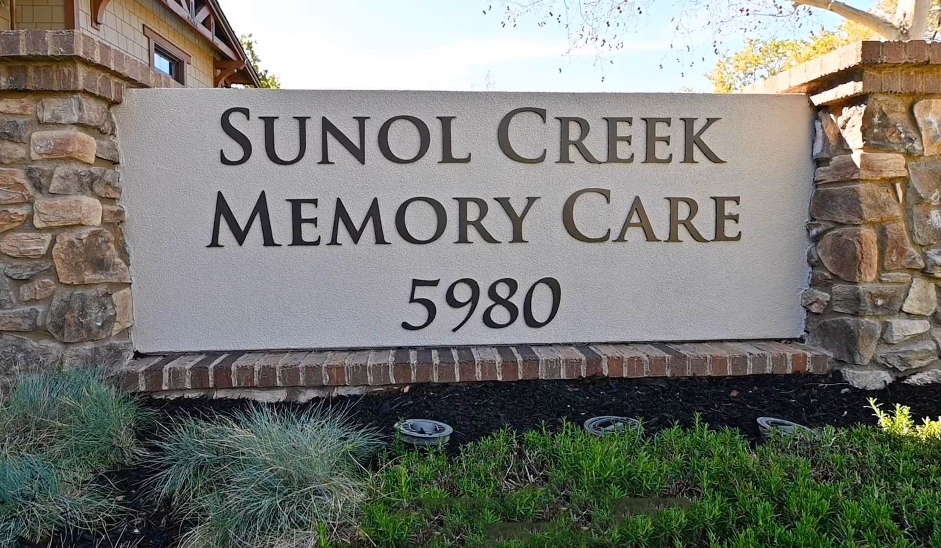 Stone and stucco entrance sign reading "Sunol Creek Memory Care 5980" with landscaping in front.