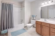 Clean, well-lit bathroom featuring a bathtub with a shower curtain, a toilet, and a wood vanity with sink and mirror.