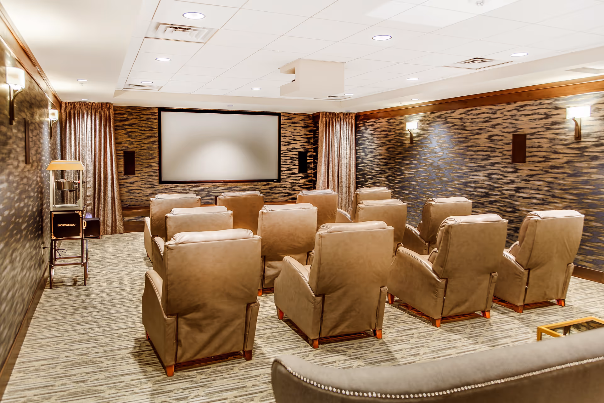 A cozy screening room with multiple beige recliner chairs arranged facing a large projection screen.
