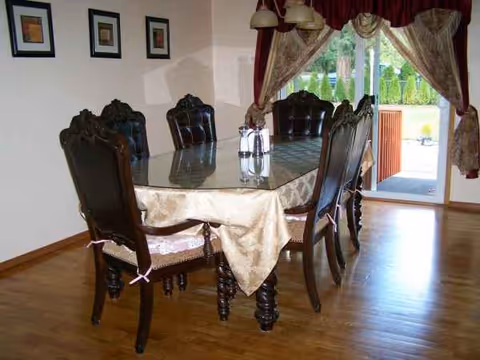 Elegant dining room with a glass-top table, ornate chairs, and draped curtains.