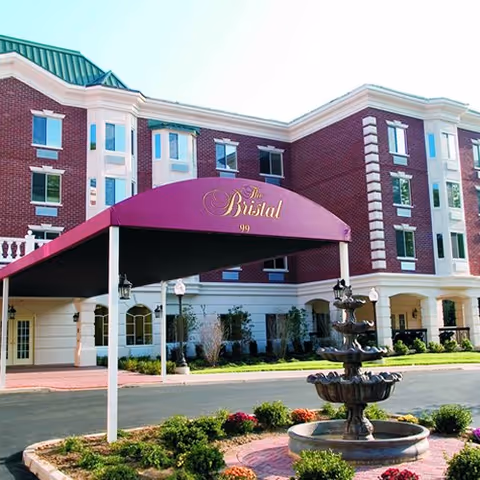 Exterior view of The Bristal Assisted Living at North Hills, with a purple canopy and fountain.