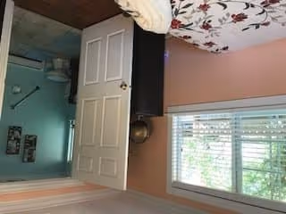 Bedroom with a floral bedspread, a window with blinds, and an open door showing an adjacent teal room.