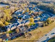 Aerial view of Blakey Hall Retirement Community showing multiple buildings surrounded by trees and parking areas, with a highway visible on the right side of the image.