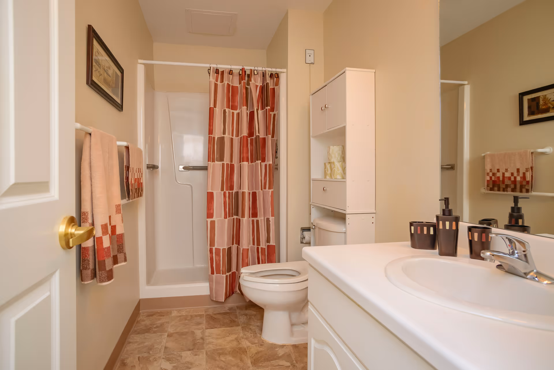 Small bathroom with a shower-tub behind a patterned curtain, toilet, white vanity sink, and a storage cabinet.