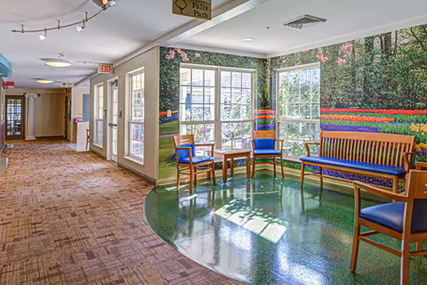 Bright interior hallway with a seating alcove of chairs and benches by large windows and a colorful garden mural.