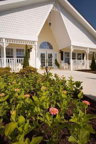 White senior living facility with a covered front porch and blooming pink flowers in foreground.
