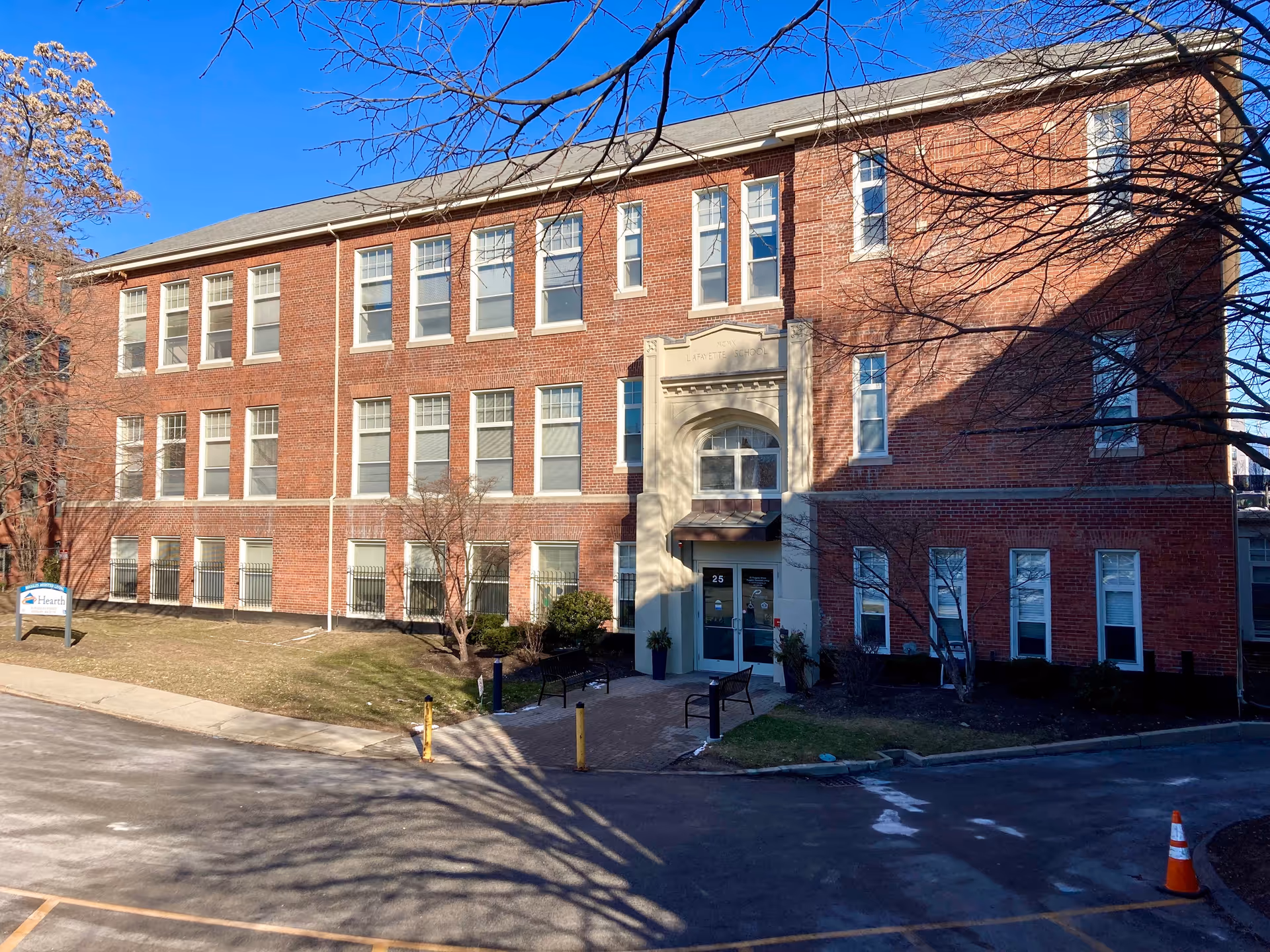 Three-story red brick building with a central arched entrance and a small parking/driveway area in front.