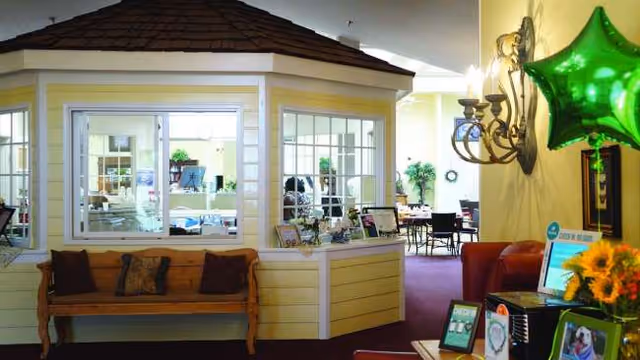 Indoor lobby with a yellow reception kiosk, seating, plants, and a chandelier.