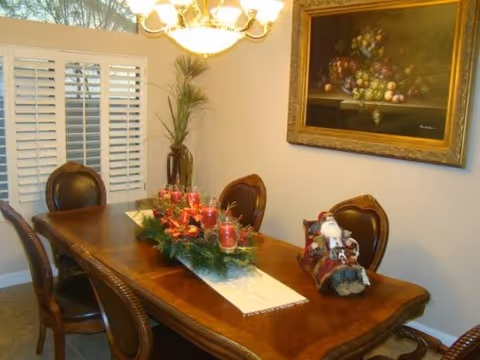 A wood dining table with chairs in a decorated dining room, featuring a holiday centerpiece and a framed painting on the wall.