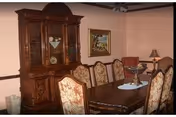 Formal dining room with a wooden dining table, upholstered chairs, and a china cabinet against a pink wall.