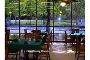 Dining area with tables covered in green tablecloths and chairs, large windows showing outdoor greenery and trees, labeled as Fine Dining Room.