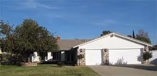 Single-story building with a two-car garage, lawn, and trees in the front yard.