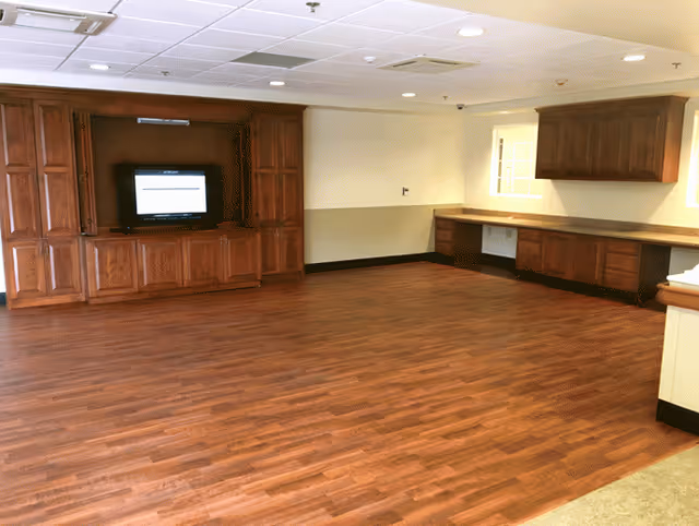 Spacious interior common room with wood flooring, built-in wooden cabinets and an entertainment center with a TV.