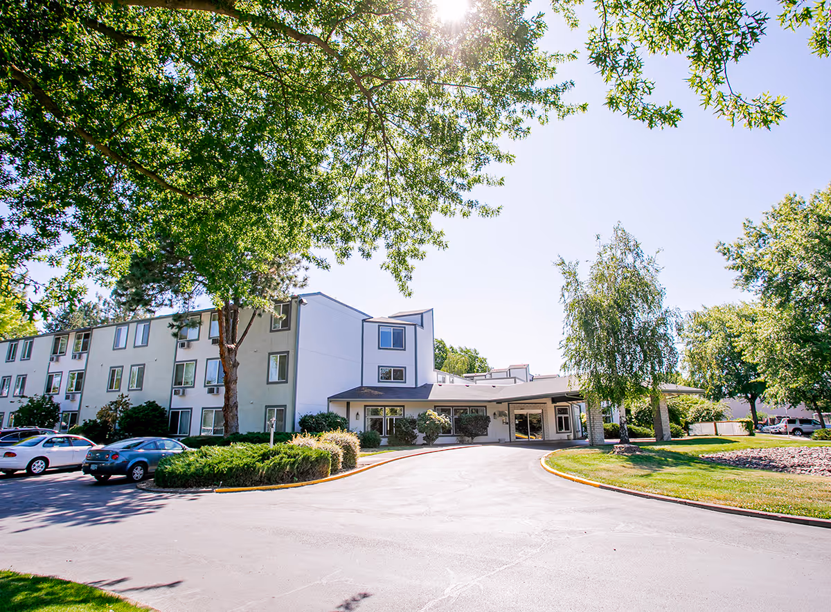 Exterior view of Rogue River Estates senior living facility with a front entrance, driveway, and surrounding trees.