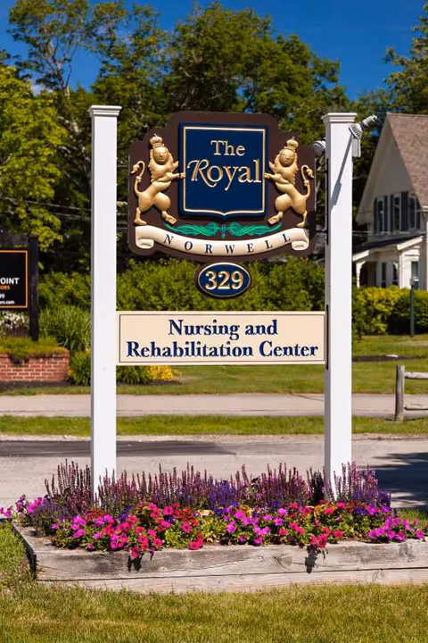 Exterior sign for The Royal Norwell Nursing and Rehabilitation Center with colorful flowers.
