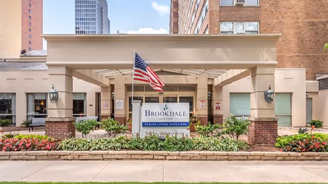 Front entrance of Brookdale Lake View senior living with a sign, American flag, and landscaped planters.