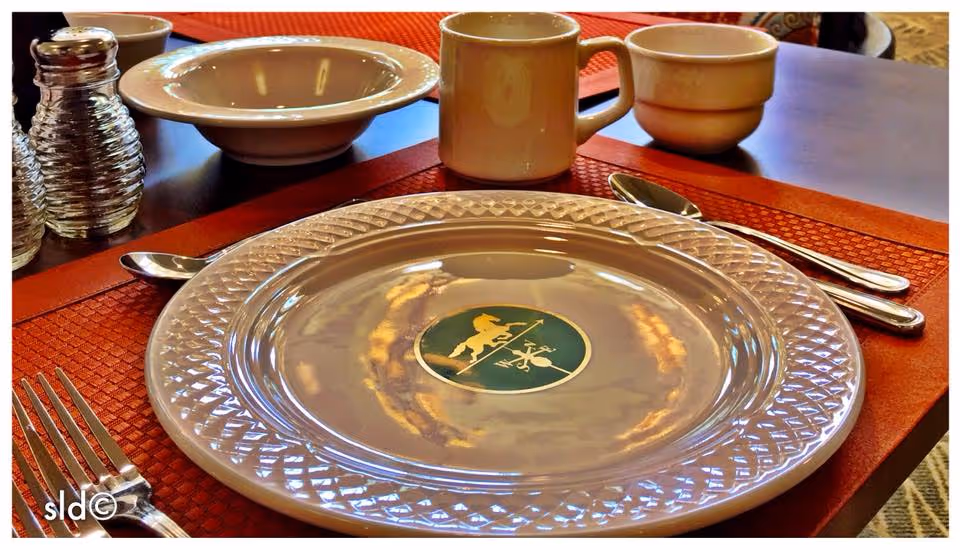 Close-up of a dining place setting with a decorative plate, mug, bowls, utensils and a salt shaker on a placemat.
