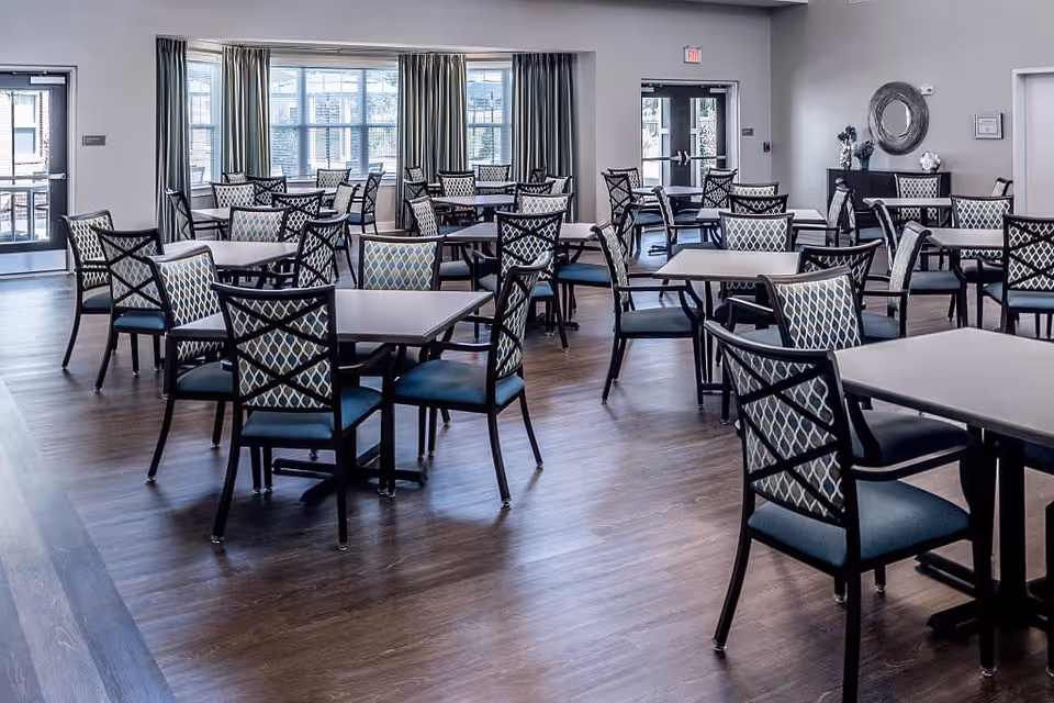 Spacious dining room with multiple tables and patterned cushioned chairs on wood flooring and large windows.