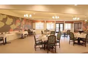 Bright dining room with round tables and upholstered chairs, chandeliers, and a large decorative wall mural.