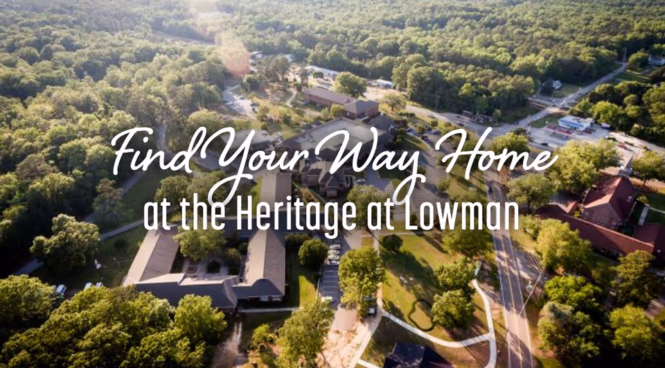 Aerial view of The Heritage at Lowman facility surrounded by dense green trees and roads, with sunlight casting a warm glow over the buildings and landscape.