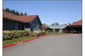 Front exterior of a single-story senior living facility with red-tiled roofs, landscaped shrubs, and a paved driveway.
