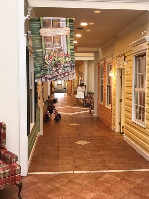 Hallway inside Seneca Lake Terrace with storefront-style room facades, tiled floor, seating, and mobility walkers.