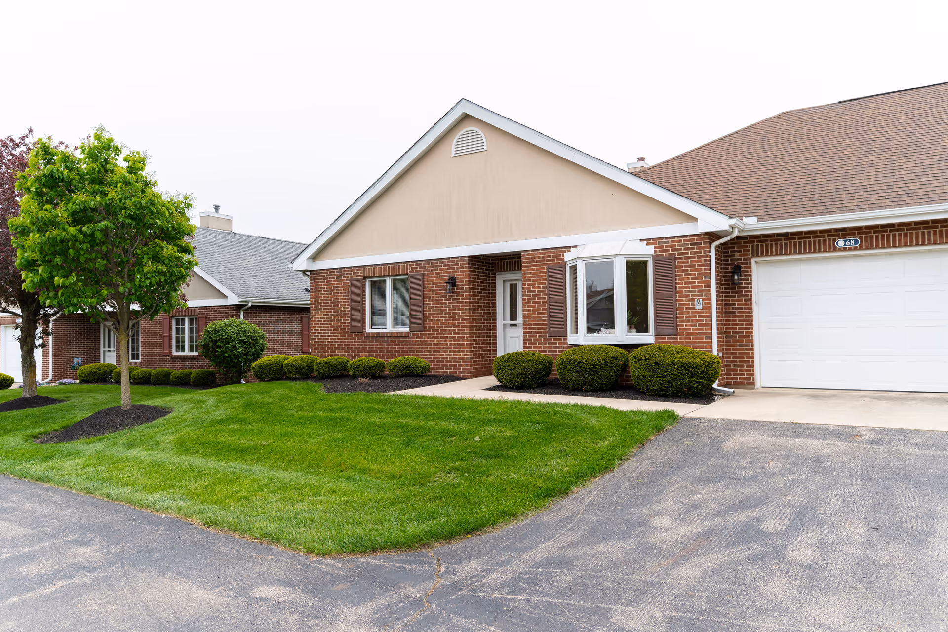 Front exterior of a single-story brick senior living home with a garage, bay window, and manicured lawn.