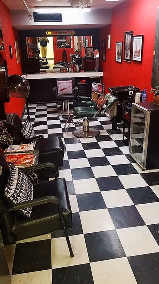 Interior of a small hair salon with red walls, black-and-white checkered floor, styling chairs, mirrors and waiting chairs.