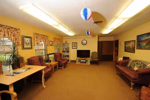 Common living room in a senior facility with sofas, chairs, plants, balloons, and a TV.